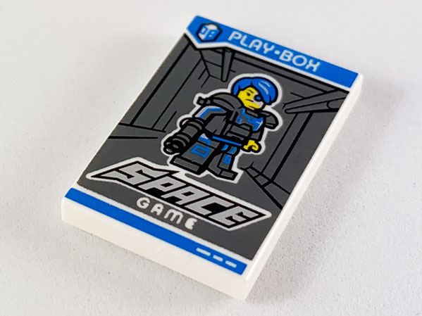 Display of LEGO part no. 26603pb046 Tile 2 x 3 with 'PLAY-BOX', 'SPACE GAME' and Collectible Minifigures Series 16 Cyborg Pattern  which is a White Tile 2 x 3 with 'PLAY-BOX', 'SPACE GAME' and Collectible Minifigures Series 16 Cyborg Pattern 