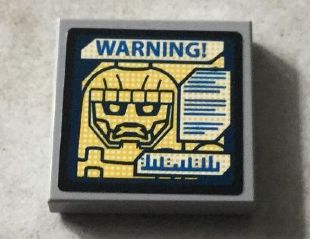 Display of LEGO part no. 3068bpb0935 Tile 2 x 2 with Groove with Sentinel Face and Blue 'WARNING! on Screen Pattern (Sticker), Set 76022  which is a Light Bluish Gray Tile 2 x 2 with Groove with Sentinel Face and Blue 'WARNING! on Screen Pattern (Sticker), Set 76022 