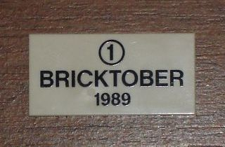 Display of LEGO part no. 87079pb0010 Tile 2 x 4 with Black '1' in Circle and 'BRICKTOBER 1989' Pattern  which is a White Tile 2 x 4 with Black '1' in Circle and 'BRICKTOBER 1989' Pattern 